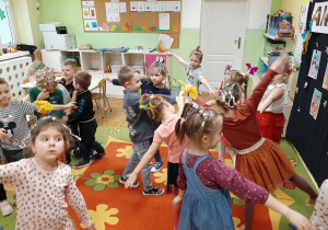 Dzieci w rozsypce tańczą na dywanie do wesołej piosenki.