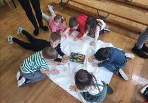 Przedszkolaki wspólnie kolorują alpakę na dużym arkuszu papieru