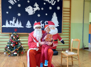 Mikołaj trzyma na kolanach chłopca z młodszej grupy podczas rozdawania prezentów