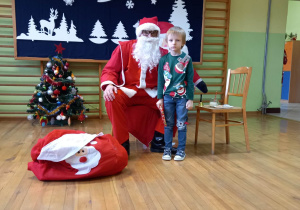 Dziecko z grupy 5-6 latków stoi z prezentem przy Mikołaju