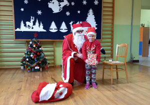 Dziewczynka z grupy 5-6 latków stoi z prezentem przy Mikołaju