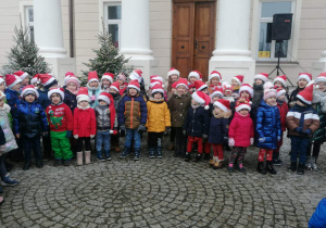 Duża grupa przedszkolaków w świątecznych strojach stoi na tle pałacu w parku w Starym Gostkowie, śpiewają.