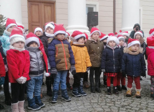 Dzieci ubrane w czapki Mikołaja stoją przed wejściem do pałacu w Starym Gostkowie
