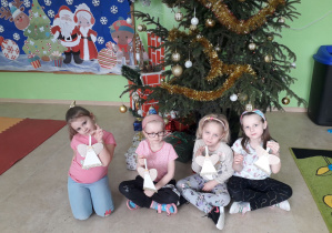 Dziewczynki na tle ubranej choinki prezentują ozdobę świąteczną- aniołka.