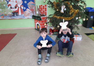 Chłopcy na tle ubranej choinki prezentują ozdobę świąteczną- aniołka.