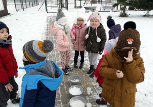 Zabawy badawcze dzieci ze śniegiem na placu przedszkolnym.