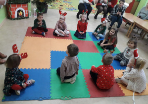 Dzieci na dywanie uczestniczą w zajęciu, obok obserwujący zajęcie rodzice.