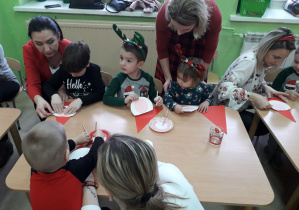 Dzieci wspólnie z rodzicami wykonują papierowego Mikołaja.