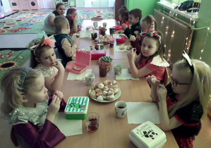 Dzieci przy stolikach zajadają karnawałowe smakołyki.