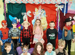 Dzieci przebrane za postacie z bajek pozują na tle karnawałowej, kolorowej dekoracji.