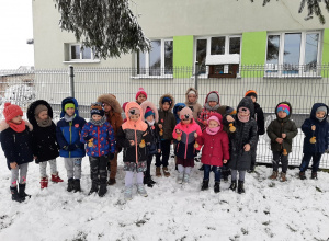 Dzieci na dworze przed przedszkolem prezentują kulki z ziaren dla ptaków.