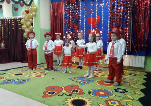 Dzieci w pięknych kostiumach, na tle walentynkowej dekoracji prezentują występ artystyczny.