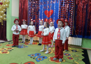 Dzieci w pięknych kostiumach, na tle walentynkowej dekoracji prezentują występ artystyczny.