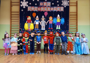Dzieci z grupy młodszej stoją na tle dekoracji przedszkolnej
