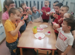 Dzieci stoją przy stoliku i trzymają pączka z masy solnej