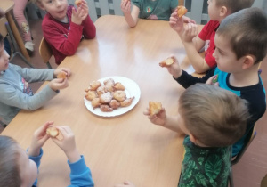 Dzieci siedzą przy stoliku i jedzą pączki