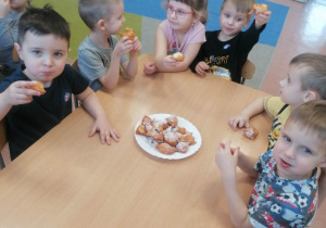 Przedszkolaki siedzą przy stoliku i jedzą pączki
