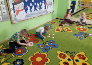 Grupa dzieci na dywanie układa pocięty obrazek pączka w całość.