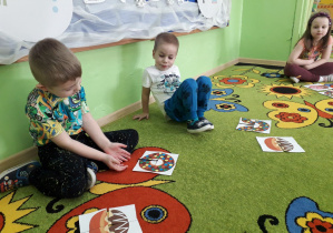 Grupa dzieci na dywanie układa pocięty obrazek pączka w całość.