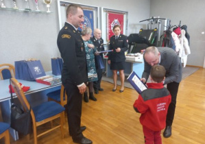 Chłopiec w stroju małego strażaka odbiera nagrodę.
