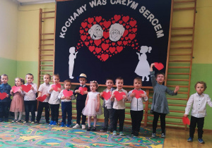 Przedszkolaki stoją z sercami na tle dekoracji przedszkolnej