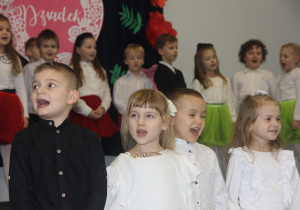 Na pierwszym planie kilkoro dzieci z grupy 3,4,5 latków śpiewa piosenkę. W tle pozostałe dzieci.