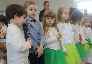 Dzieci z grupy 3,4,5 latków stoją w rzędzie i recytują do mikrofonu wiersze.