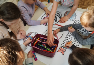 Dziewczynki z grupy 5,6 latków siedzą przy stoliku, kolorują obrazek tematyczny.