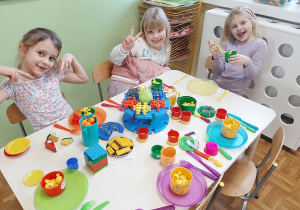 Grupa dziewczynek siedzi przy stoliku, prezentuje tłustoczwartkową ucztę przygotowaną z klocków w kąciku zabaw.