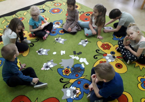 Dzieci na dywanie układają z elementów postać wilka.