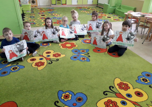 Dzieci na dywanie prezentują wykonane prace plastyczne "Las Czerwonego Kapturka."