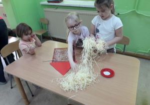 Dziewczynki przy stoliku konstruują słomiany domek z baśni "Trzy świnki".
