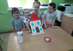 Grupa dzieci prezentuje drewniany domek z baśni "Trzy świnki".