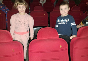 Dzieci z grupy młodszej stoją między siedzeniami w kinie