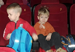 Dzieci z grupy młodszej siedzą na czerwonych fotelach w kinie