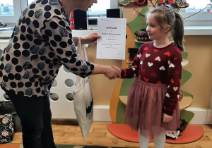 Nauczyciel gratuluje dziewczynce, która zdobyła drugą nagrodę w konkursie.