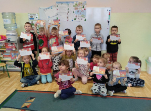 Dzieci z grupy 3,4,5 latków pozują do fotografii prezentując upominki, które przesłał wraz z listem Święty Mikołaj. W tle widoczny list od Mikołaja.