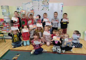 Dzieci z grupy 3,4,5 latków pozują do fotografii prezentując upominki, które przesłał wraz z listem Święty Mikołaj. W tle widoczny list od Mikołaja.