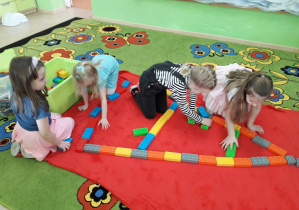 Dziewczynki na dywanie konstruują Wieżę Eiffla z kloców.