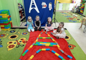 Dziewczynki na dywanie prezentują zbudowaną z klocków Wieżę Eiffla.