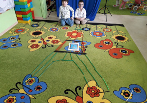 Chłopcy na dywanie prezentują zbudowaną ze słomek konstrukcyjnych Wieżę Eiffla.