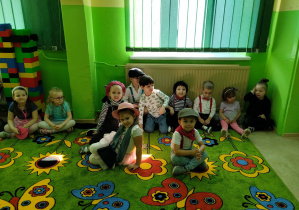 Dzieci na dywanie prezentują się w kostiumach mody francuskiej.