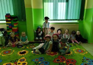 Dzieci na dywanie prezentują się w kostiumach mody francuskiej.