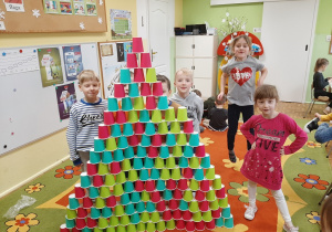 Grupa dzieci buduje z kolorowych kubków jednorazowych wieżę.