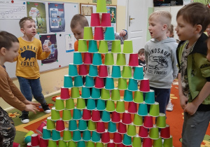Grupa dzieci buduje z kolorowych kubków jednorazowych wieżę, kolejne ujęcie.
