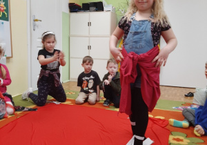 Pokaz przedszkolnej mody. Dziewczynka prezentuje spódniczkę z różowego materiału.