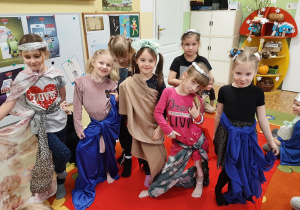 Pokaz przedszkolnej mody. Grupa dziewczynek pozuje w wymyślonych przez siebie strojach.