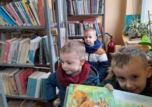Dzieci trzymają książki w bibliotece. W tle regały z książkami