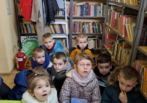 Przedszkolaki siedzą w bibliotece słuchają pani bibliotekarki