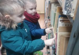 Chłopcy stoją przy regale z książkami i pokazują książki
